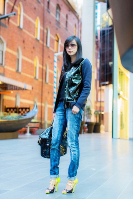 With blue shirt, patent leather vest, cuffed jeans, yellow and black high heels and sunglasses