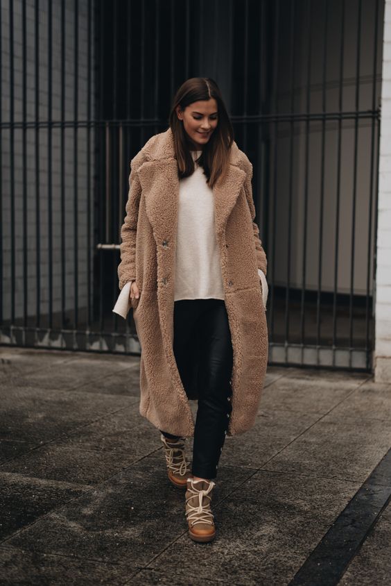 a white sweater, black leather pants, brown winter boots and a brown teddy coat