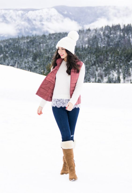 a white top with lace trim, blue jeans, a dusty pink puffer vest, beige fur boots, a white beanie