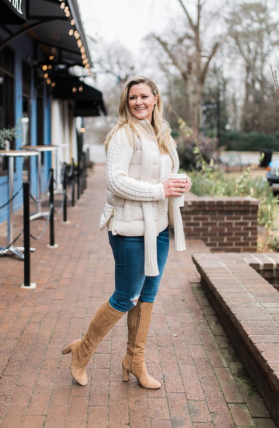 blue ripped jeans, a creamy cable knit sweater, a creamy puffer vest, beige knee boots and a creamy scarf