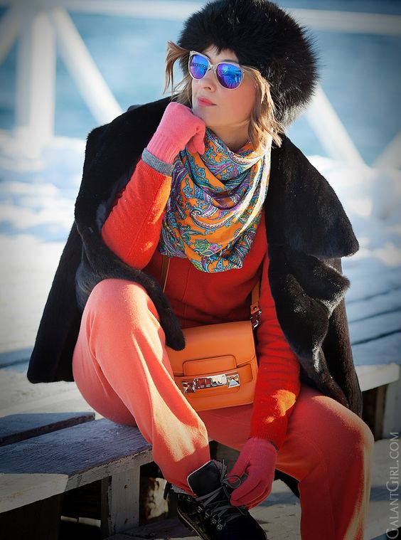 coral pants, an orange sweater, a black fur capelet, black sneakers and a fur hat, a printed scarf and pink gloves