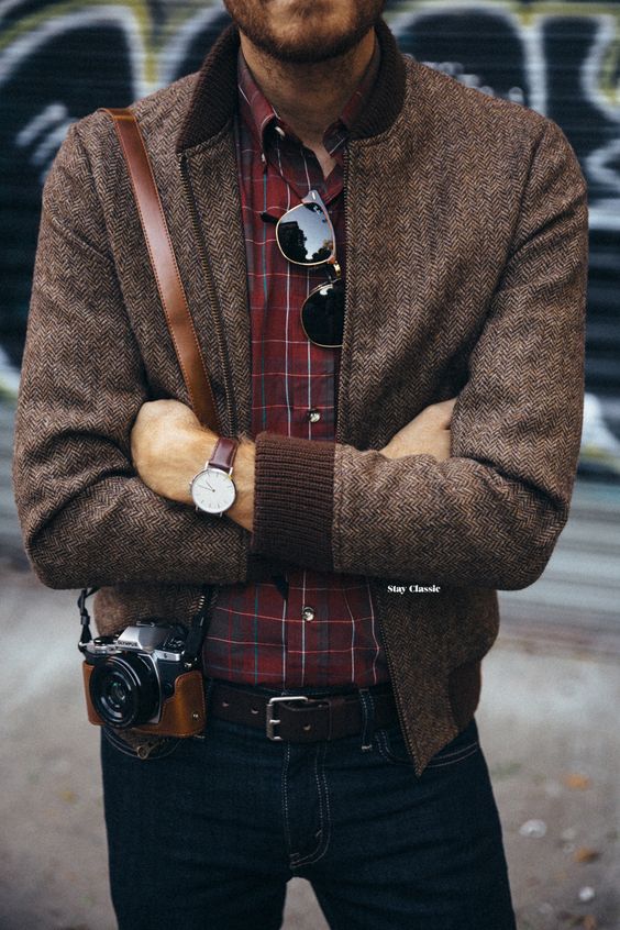 a vintage-inspired look with navy jeans, a red plaid shirt, a brown bomber jacket and a vintage camera