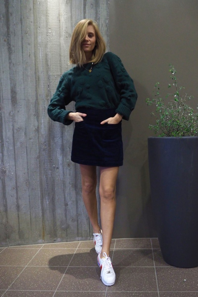 A navy velvet mini skirt with pockets, a forest green sweater, white sneakers for a casual look