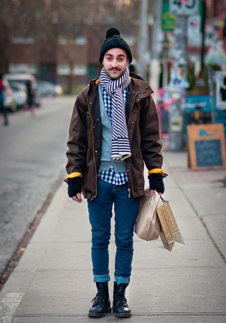 Pom pom beanie, checked shirt, light blue sweater, brown jacket, cuffed jeans, lace up boots and striped scarf