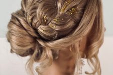 a lovely updo with a bun and large braids on top, a bump and face-framing hair plus some gold glitter for an accent
