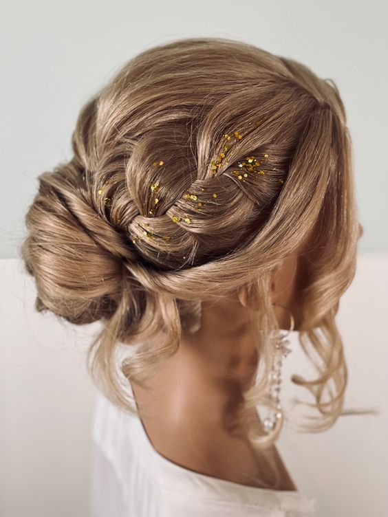a lovely updo with a bun and large braids on top, a bump and face-framing hair plus some gold glitter for an accent