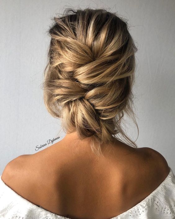 a messy woven low updo with a bump on top and some locks down is a chic and cool idea for the holidays