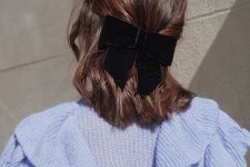 a pretty and cool half updo on medium hair, with messy waves and a black velvet bow