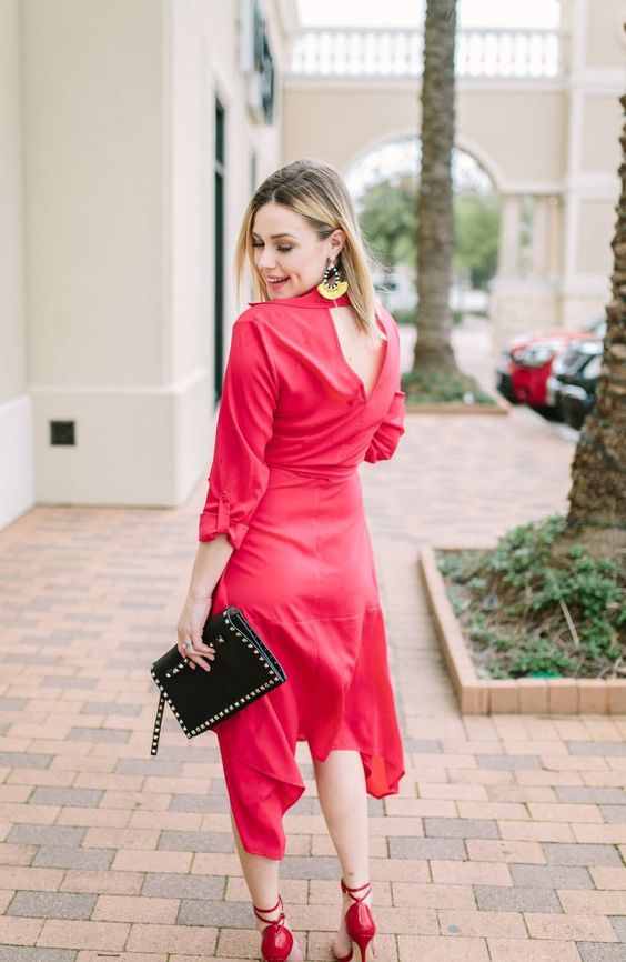 a red dress with an asymmetrical skirt and a V-cut back, red shoes and a black clutch