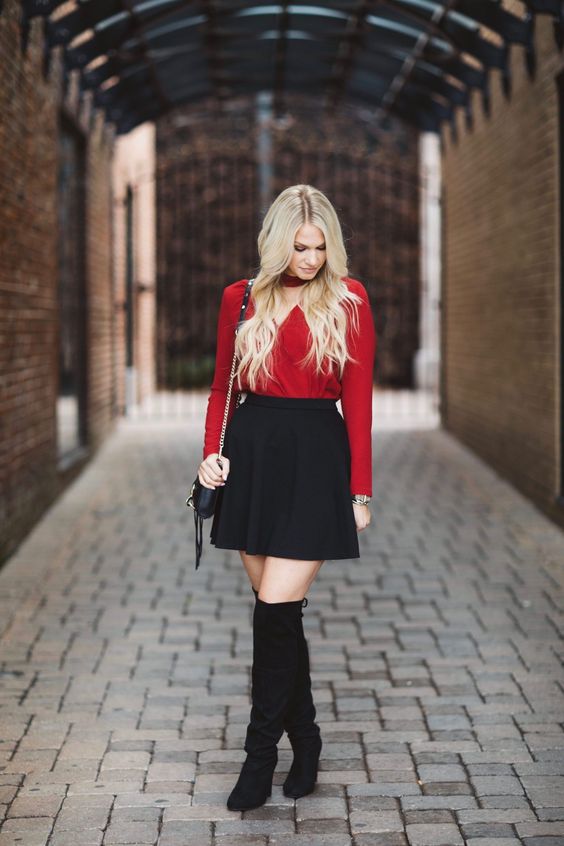 a black mini skirt, a red long sleeve top with a V-neckline, black tall boots and a little bag