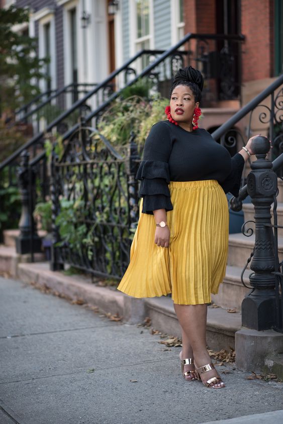 a black ruffle sleeve top, a yellow pleated skirt, metallic mules and statement earrings