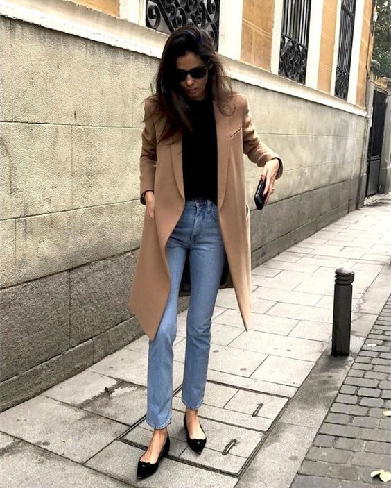 a casual and comfy look with a black tee, blue jeans, a camel coat and black pointed flats