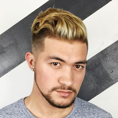 long textured slicked back hair with a high fade is accented with blonde highlights