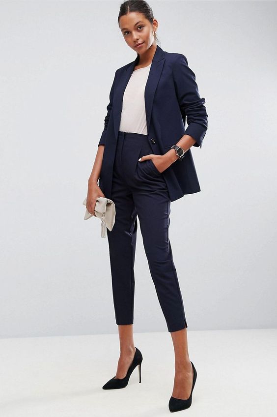 a navy pantsuit with cropped pants, a white top, black heels and a white tassel clutch