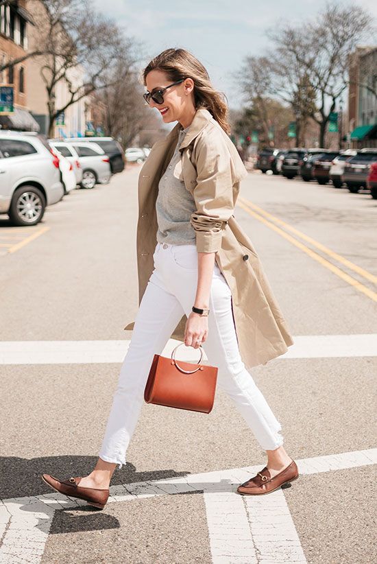 a grey tee, white jeans, a tan trench, brown loafers and a ring handle bag