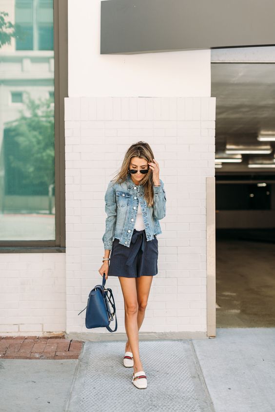 a white tee, black shorts, a blue denim jacket, white loafers and a navy bag