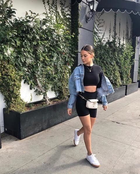 a black crop top, black cycling shorts, white sneakers, a white waist bag and a blue cropped denim jacket