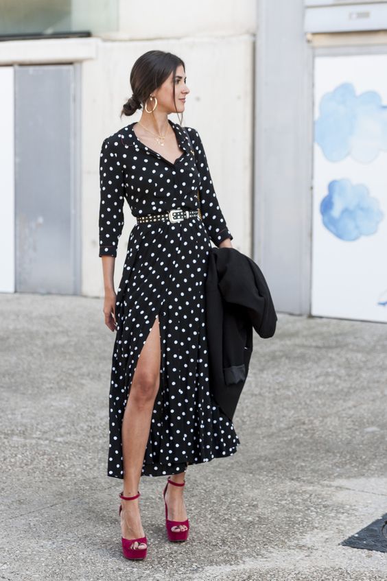 a black and white polka dot midi dress with a front slit, long sleeves, red platform shoes and a black trench