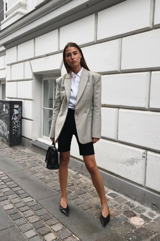 a white button down, black cycling shorts, a grey blazer, black pointed toe shoes and a black bag