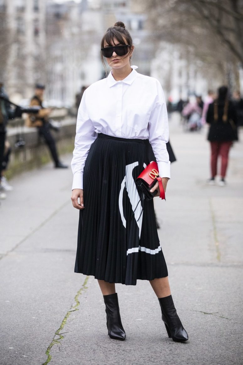 a white button down, a black and white patterned pleated midi, black boots and a catchy bag