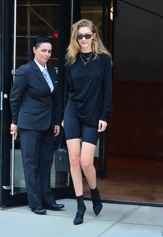 Gigi Hadid nailing bike shorts with a black top,  black sock boots and layered necklaces