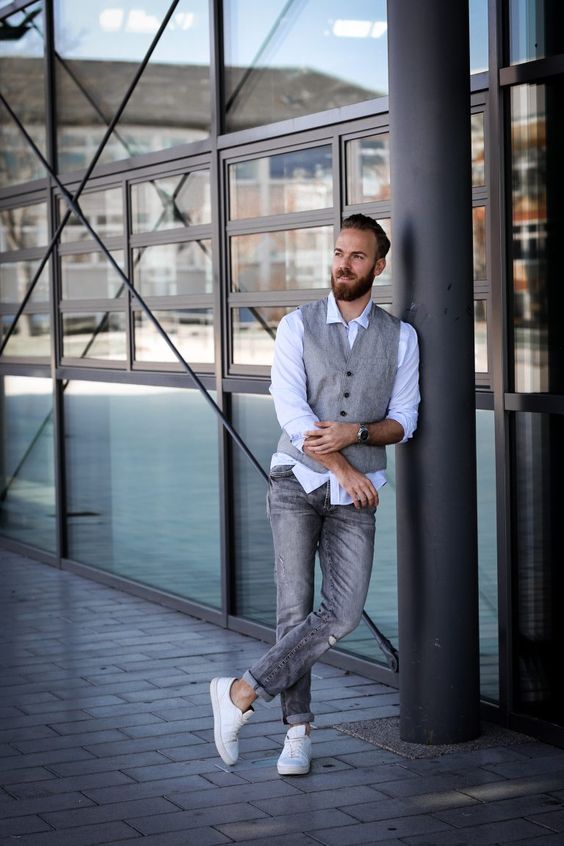 a business casual look with grey jeans, a blue shirt, a grey waistcoat and white sneakers