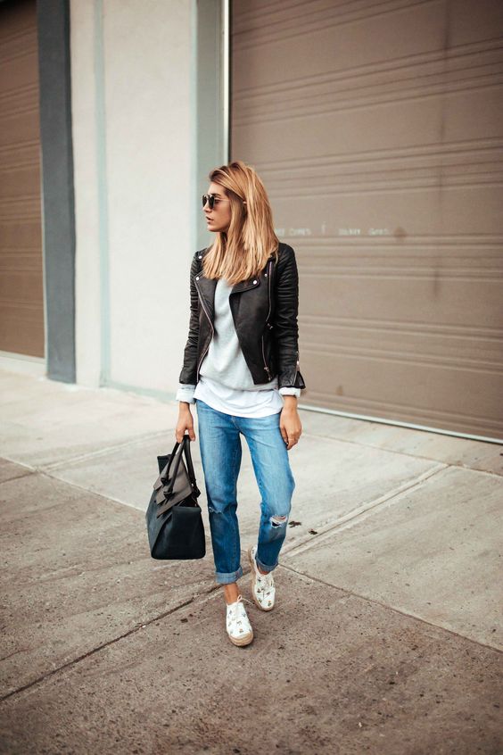 a white tee, a grey jumper, a black leather jacket, blue distressed jeans, printed sneakers and a black bag