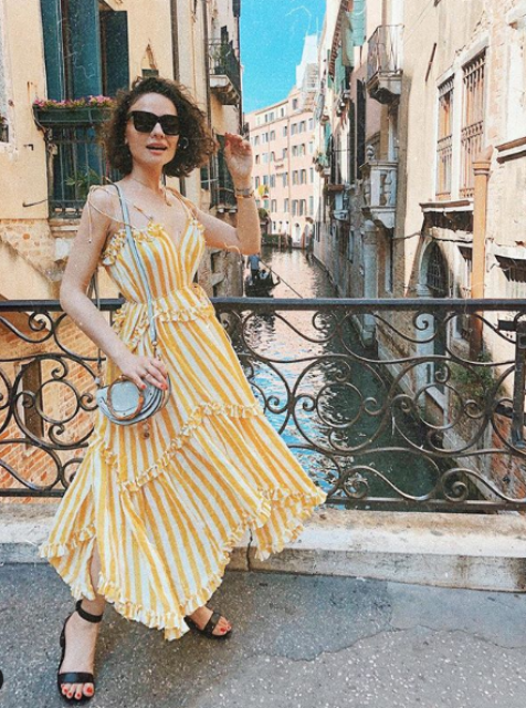 a bright striped yellow and white midi ruffle dress with spaghetti straps, black heels and a grey bag