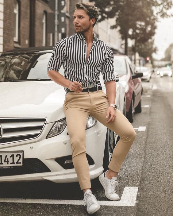 a striped black and white shirt, tan chinos, white sneakers make up a look suitable for work