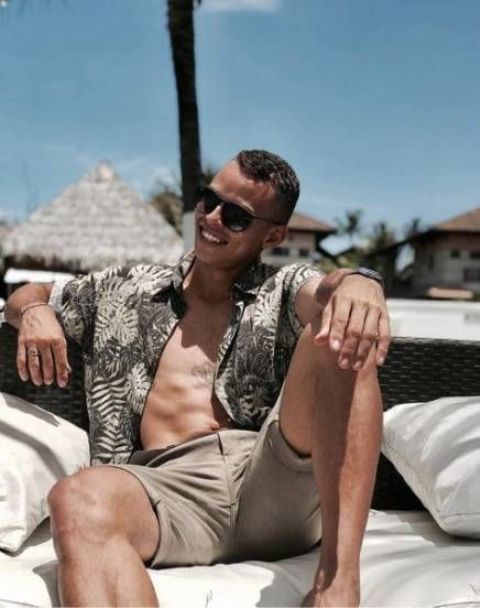 tan shorts and an unbuttoned leaf printed shirt are amazing to have a rest at the beach