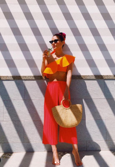bright red culottes, a bright orange crop top with a ruffle, a straw bag and shiny mules