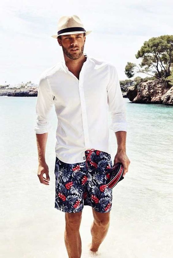a gorgeous beach look with a white shirt, navy botanical print long trunks and a straw hat