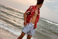 a red tropical print shirt and classic striped trunks make up a colorful and bright beach look