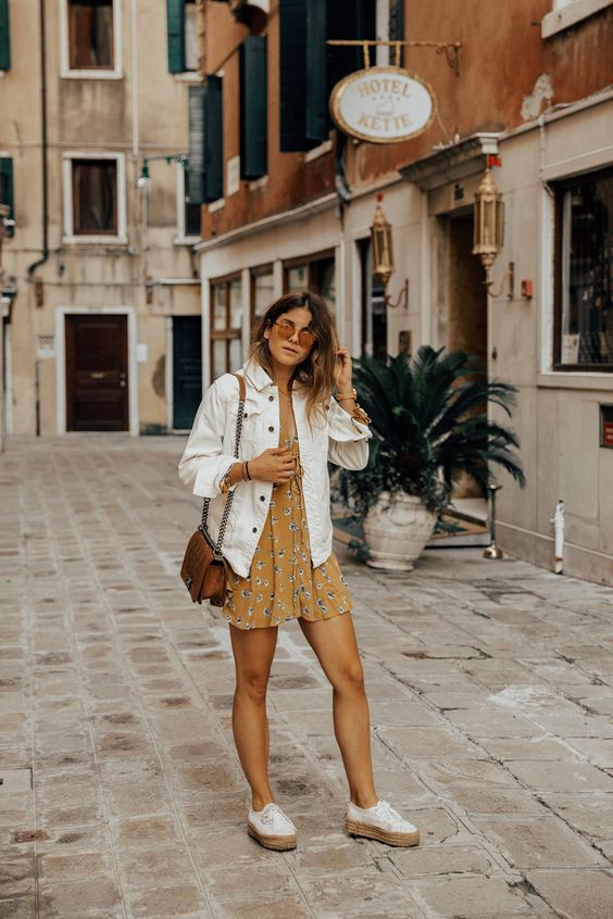 a yellow floral mini dress, an oversized white denim jacket, white sneakers and a brown bag
