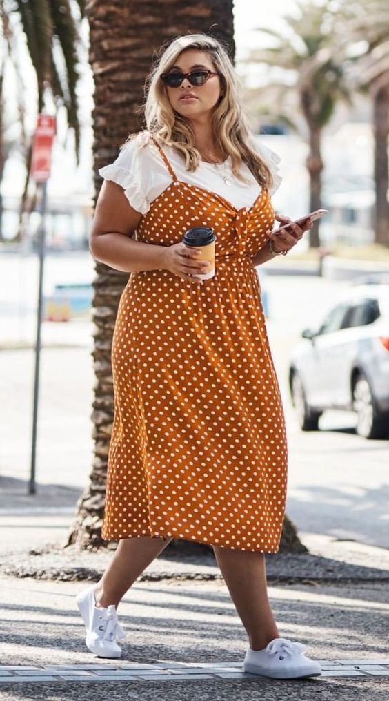 a mustard polka dot midi dress worn over a white t shirt and white sneakers for a super comfy and cute outfit