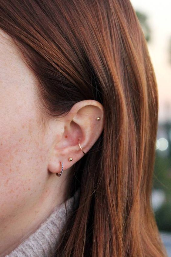 simple and stylish ear piercings with gold studs and gold and rhinestone hoops in the daith and conch