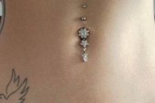 a shiny floral belly button piercing with a pendant and some studs over it