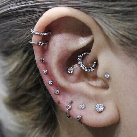 an ear all done with piercings, shiny studs and hoops along the whole helix and a rhinestone hoop in the daith