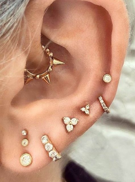 gold and shiny studs and hoops in the ear and a spiky gold hoop in the daith for a bold statement