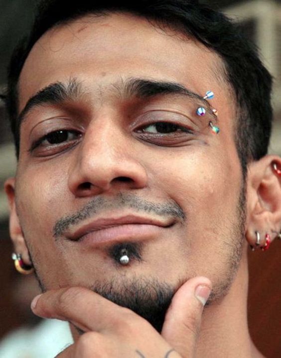 a double colorful eyebrow piercing, a chin piercing and ear piercings for a bold look