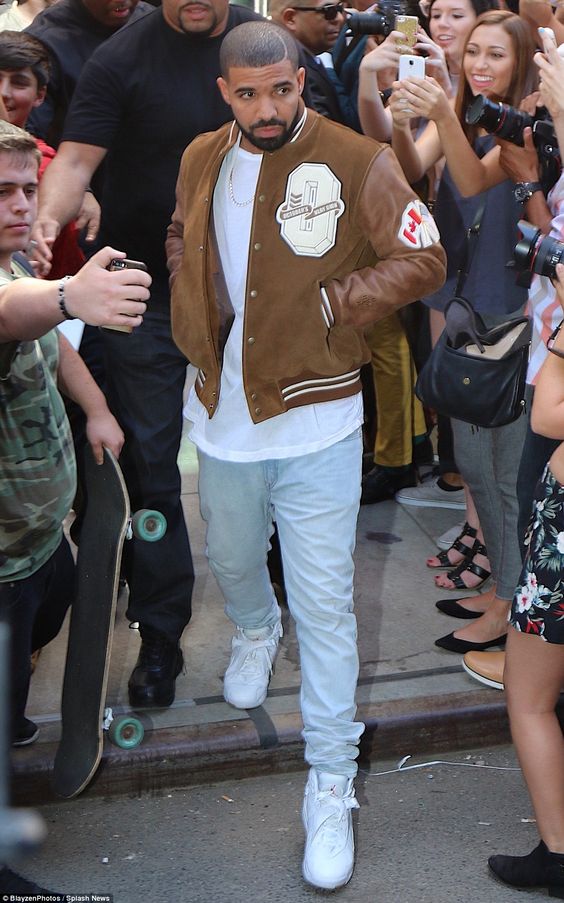 Drake wearing a white t shirt, bleached jeans, white trainers and a brown leather bomber jacket