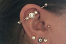 a beautifully accessorized ear with three lobe piercings, a tragus and an industrial one all done with similar studs and a bar