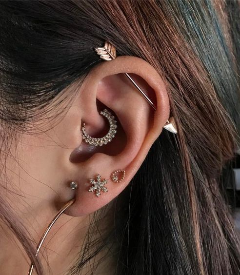 a bold ear with four lobe piercings, a daith piercing and an industrial one with shiny earrings and a bar