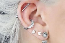 a boldly accessorized ear with three lobe piercings, a hoop in the helix and an industrial bar