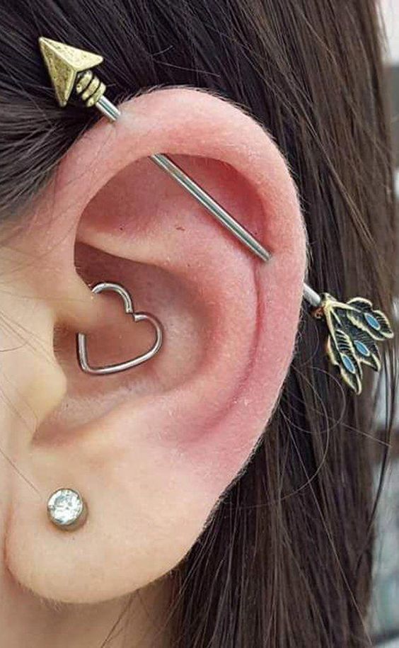 a cool look with a lobe, daith and industrial piercings accessorized with a stud, a heart hoop and an arrow bar