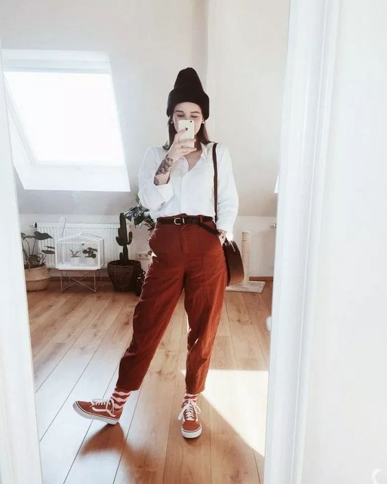 a relaxed outfit with a white shirt, rust oversized pants, orange sneakers and striped socks plus a beanie