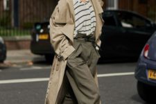 a trendy outfit with a striped oversized tee, dark green oversized pants, black boots and a tan trench