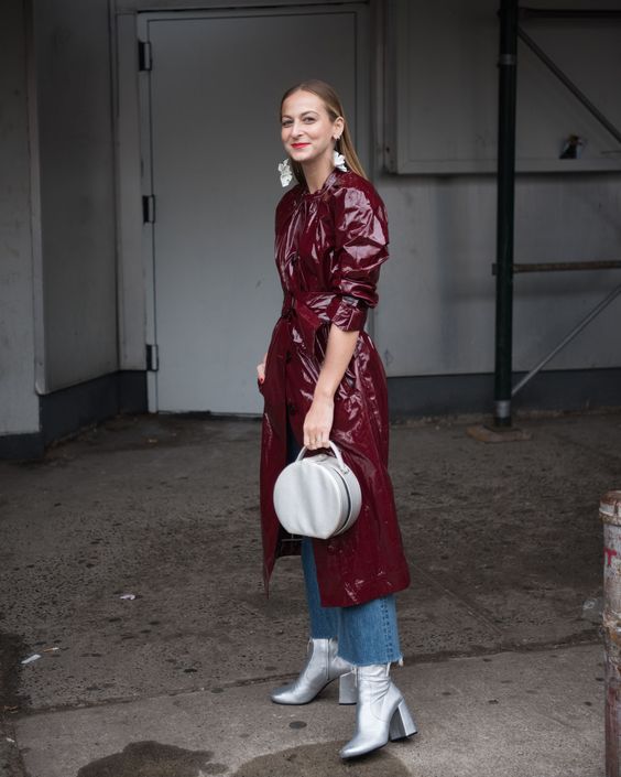 blue jeans with a raw hem, a burgundy lacquered leather trench, silver booties and a matching round bag