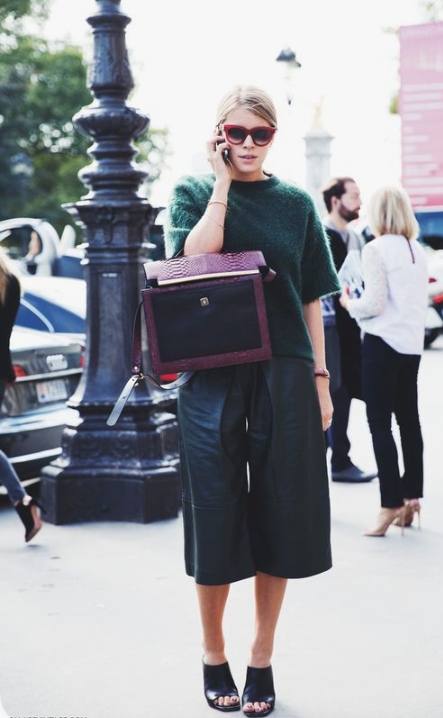 a bold and stylish look with a dark green sweater with short sleeves, black leather culottes, black shoes and a purple bag