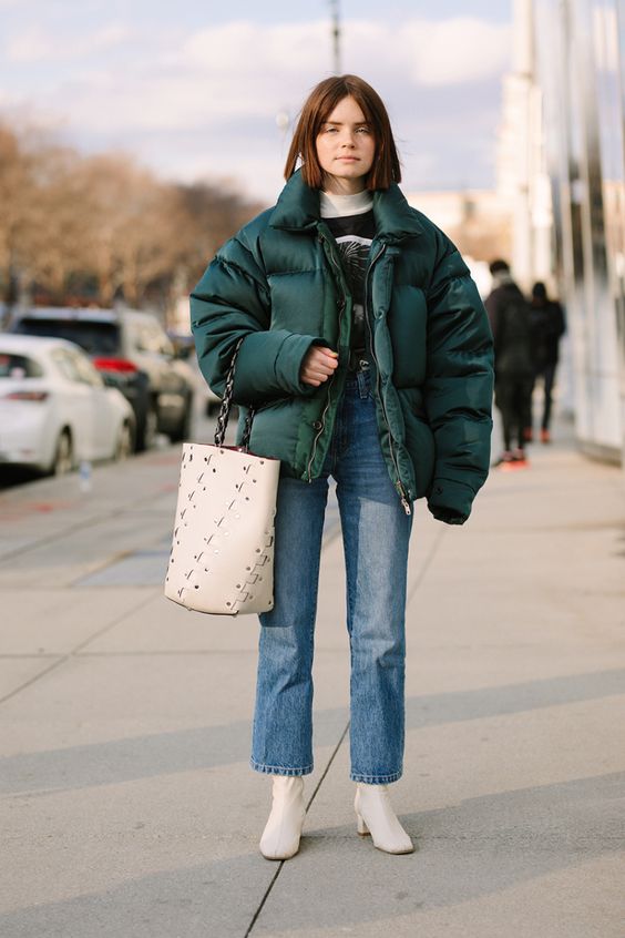 a retro-inspired look with a printed sweatshirt, blue straight jeans, white boots and a bag plus a forest green puffer jacket